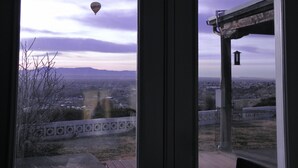 A view through a window with a hot air balloon in the sky, a distant mountain range, and a fenced area with a building in the foreground. - Secure carport, amazing Views and Reviews!  Private suite with patio.  (Albuquerque)