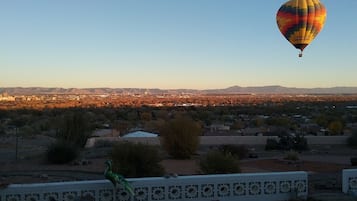 Un globo aerostático con un diseño colorido sobrevolando una zona residencial con casas y vegetación escasa.