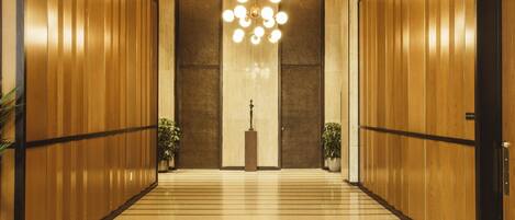 A hallway with wooden paneling, a central chandelier, and potted plants.