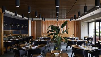 Ein modernes Restaurant mit mehreren Essplätzen, schwarzen Stühlen und Pendelleuchten.