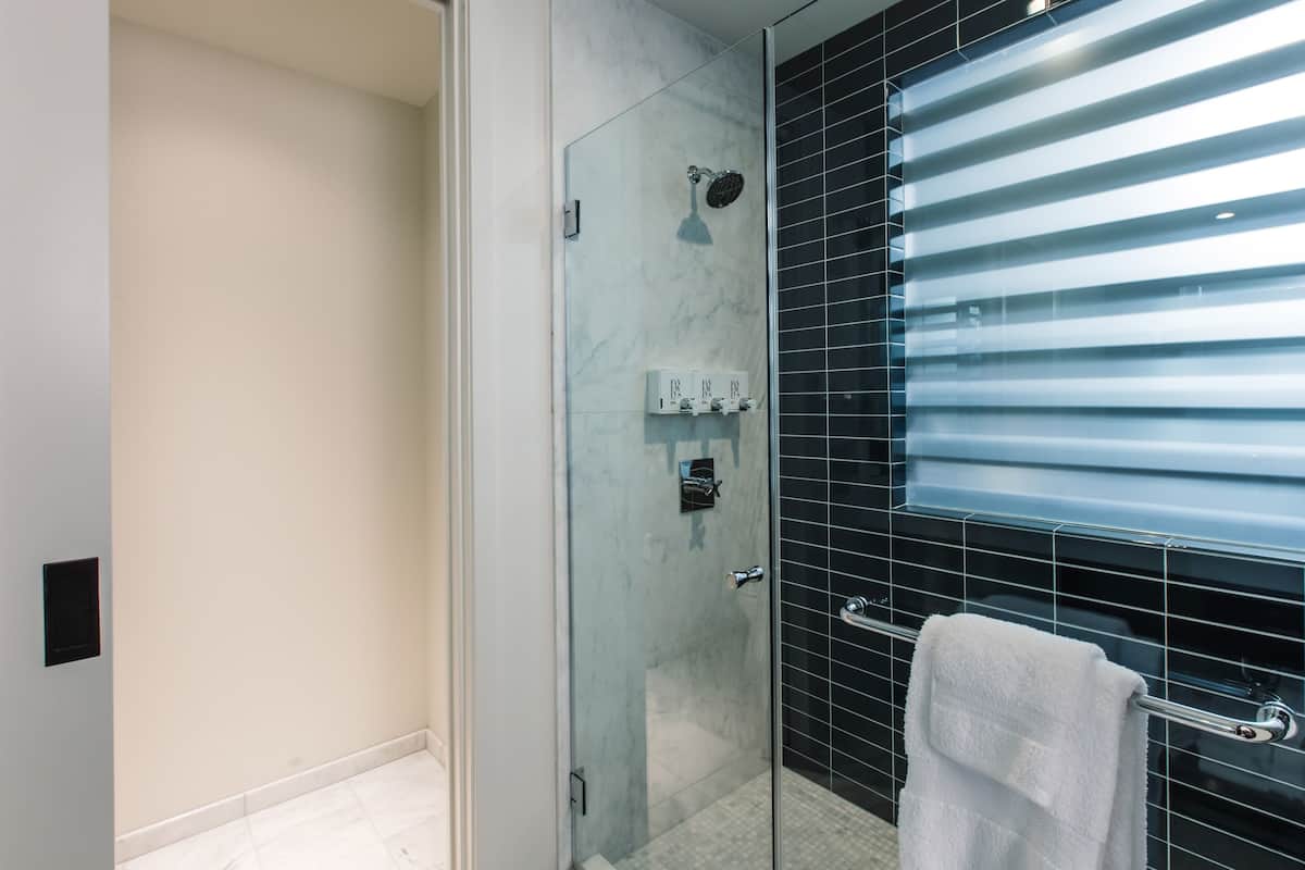 A modern bathroom with a glass shower enclosure, a white towel on a rack, and a black-tiled wall.