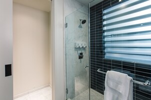 Un baño moderno con cabina de ducha de vidrio, una toalla blanca en un perchero y una pared revestida de baldosas negras.