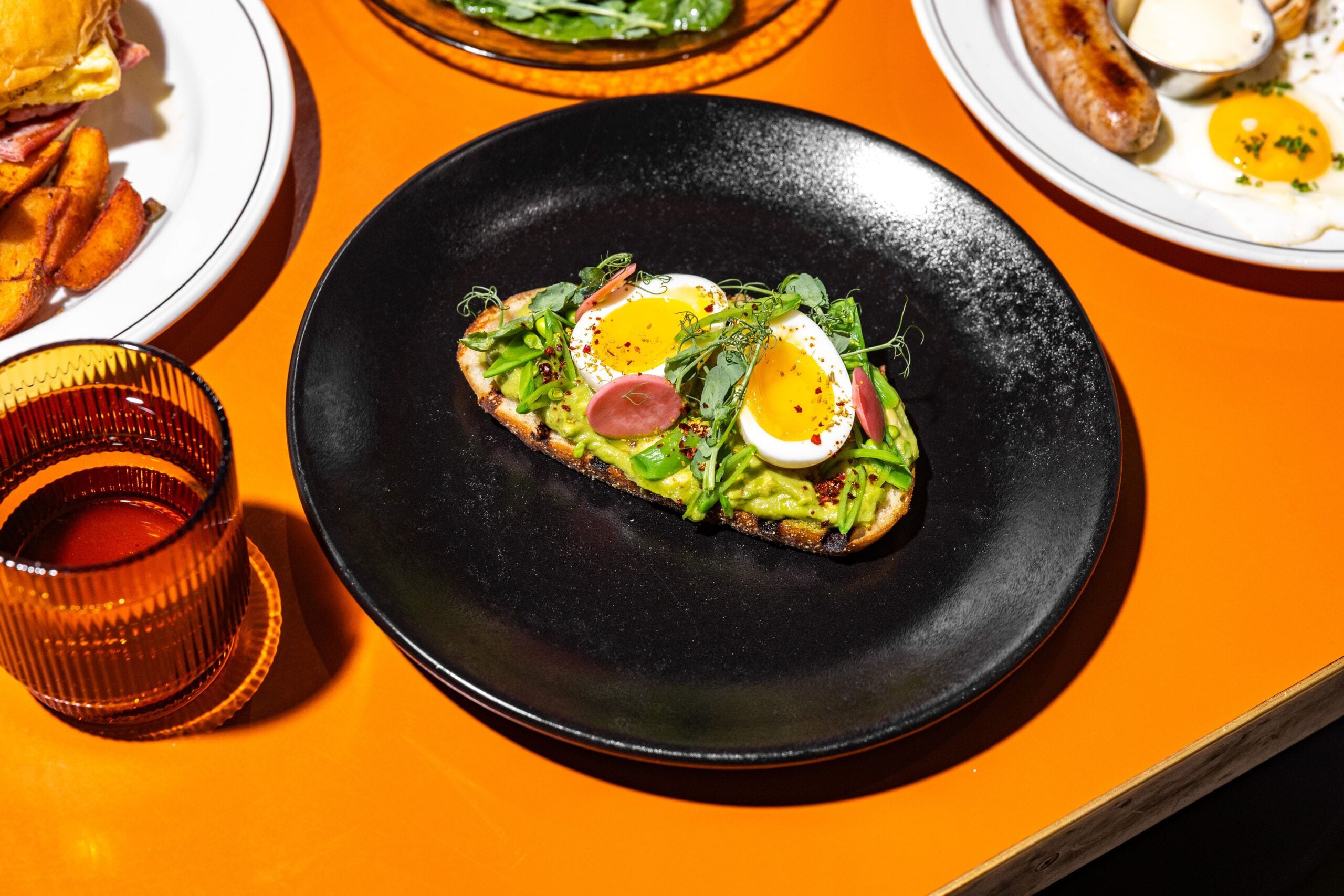 A black plate with a sandwich on an orange table.
