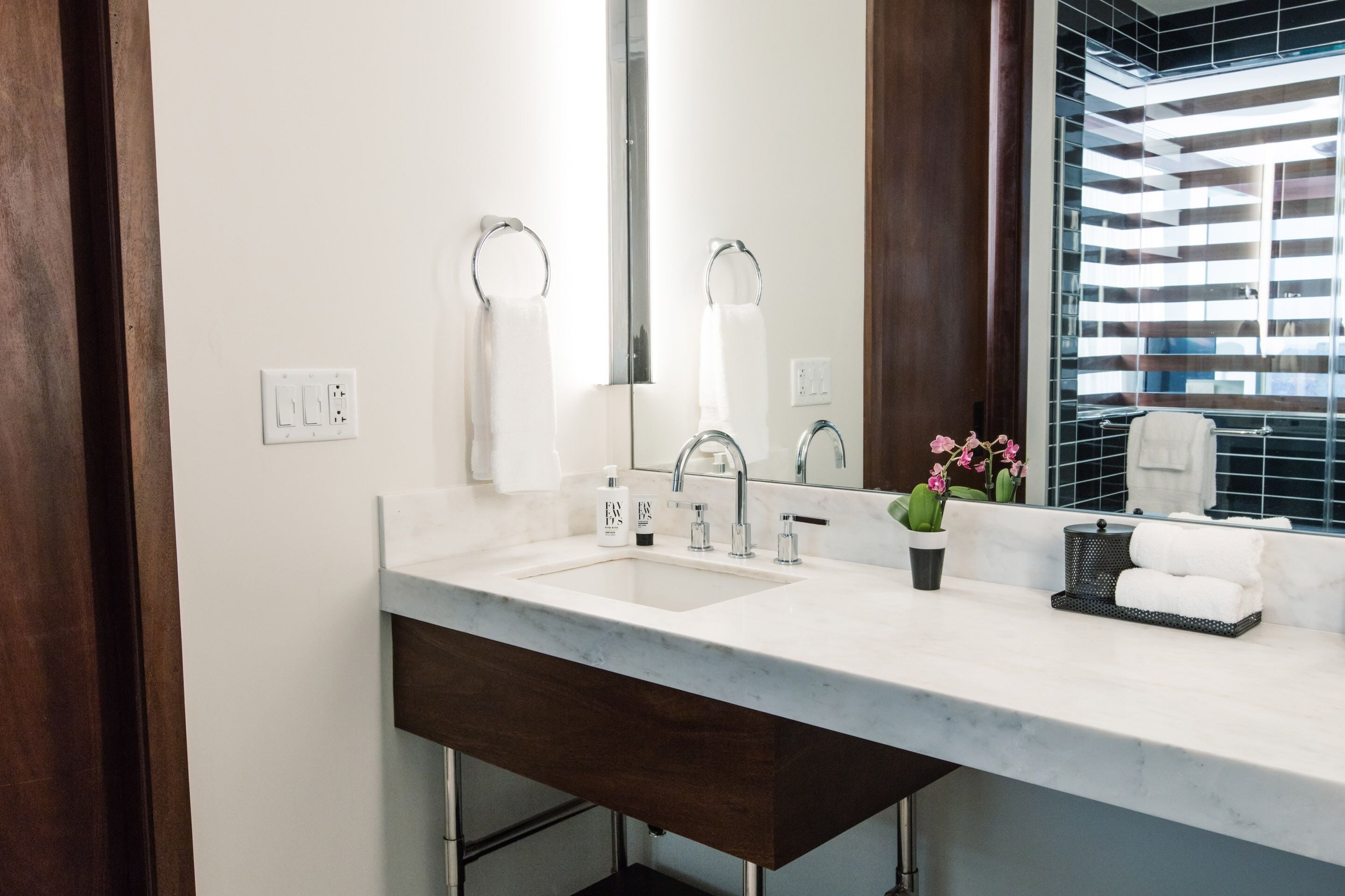 A modern bathroom with a marble sink, a large mirror, and a potted orchid.