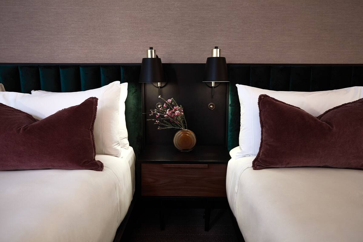 A hotel room with two beds, a nightstand with lamps, and a vase with flowers.