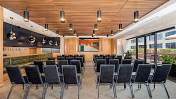 A conference room with rows of chairs, a wooden ceiling, and a large screen displaying the hotel name.