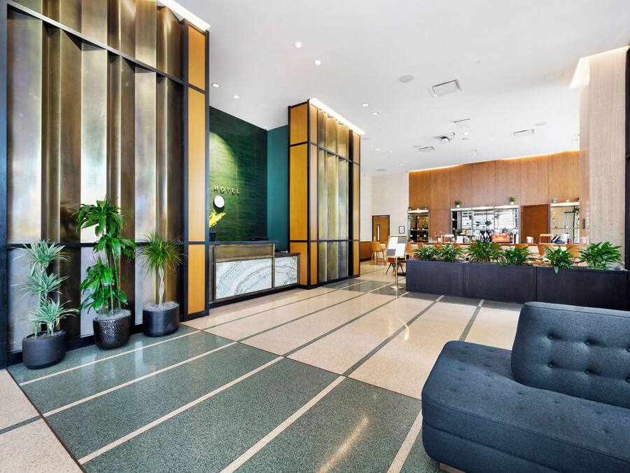 A modern hotel lobby with a reception desk, seating area, and a kitchen in the background.
