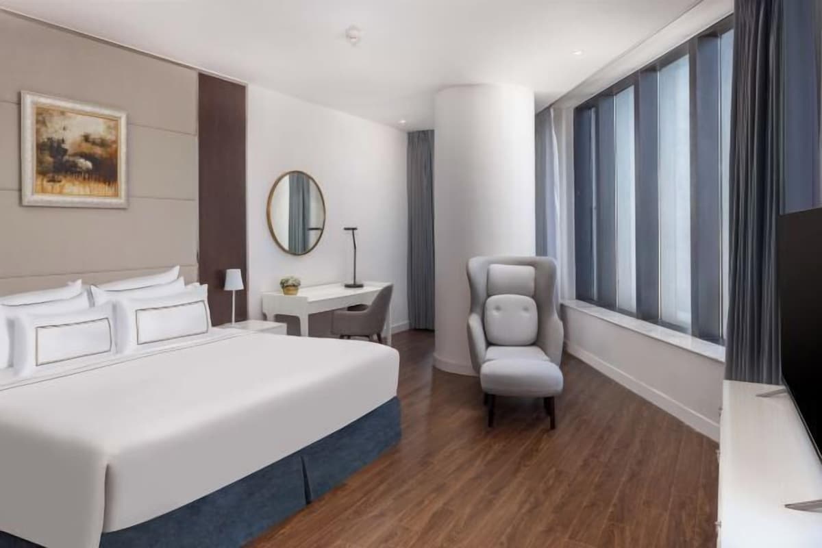 A hotel room with a large bed, a desk, a chair, a TV, and a window with curtains.