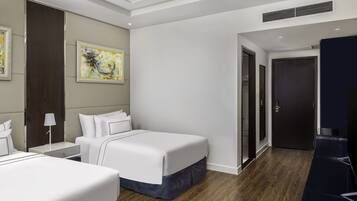 A modern hotel room with two beds, a desk, a lamp, and a painting on the wall.