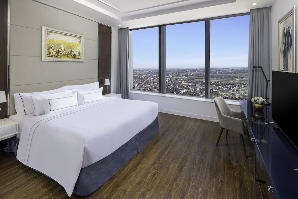 Ein Hotelzimmer mit einem großen Bett, einem Schreibtisch, einem Stuhl und einem großen Fenster mit Blick auf die Stadt.