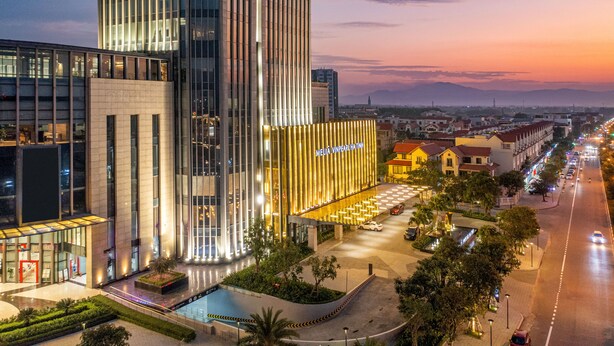Un hôtel moderne doté d’une façade verticale imposante, d’un vaste espace extérieur aménagé et offrant une vue sur le paysage urbain environnant.