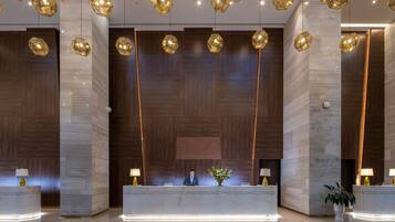 A reception area with a modern design, featuring a marble reception desk, wooden panel walls, and geometric pendant lighting.