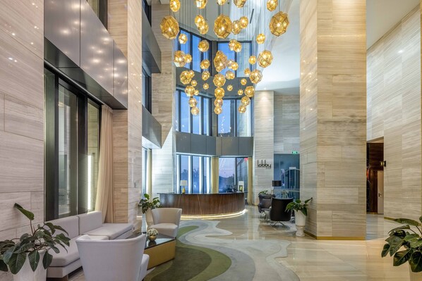 A modern lobby with a reception desk, seating area, and a unique ceiling light fixture.