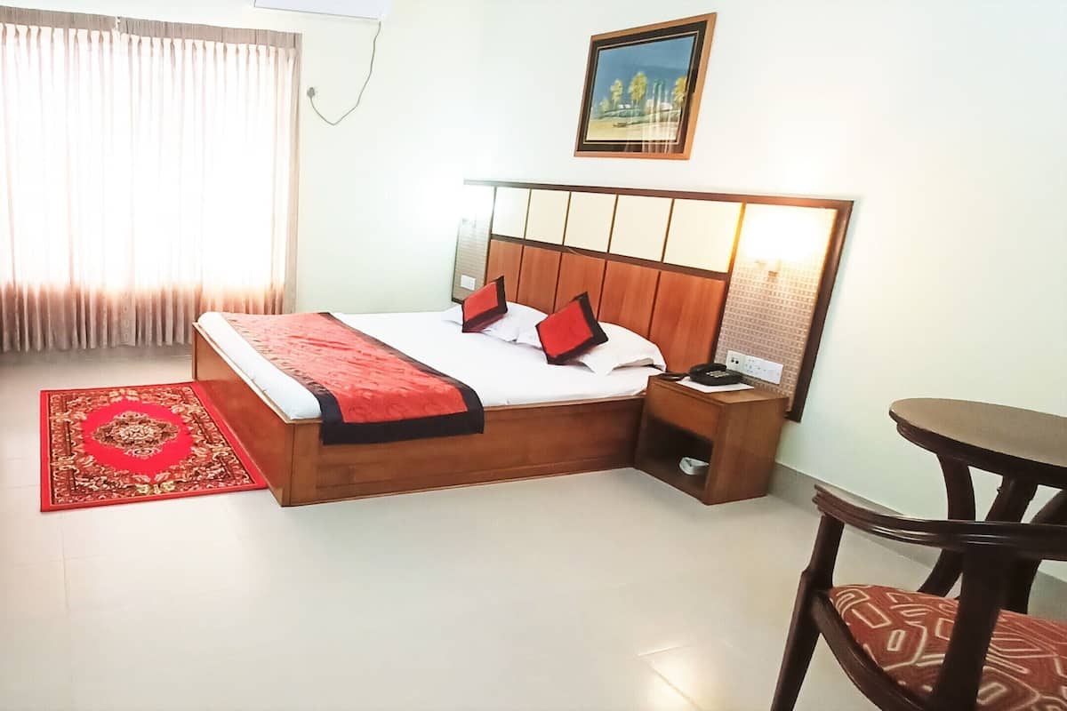 A hotel room with a bed, bedside table, desk, chair, and a red rug.