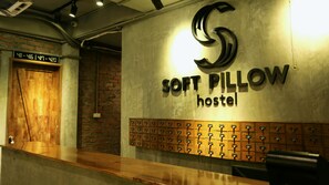 A reception desk with a sign for 'SOFT PILLOW hostel' and a wall of storage lockers below.