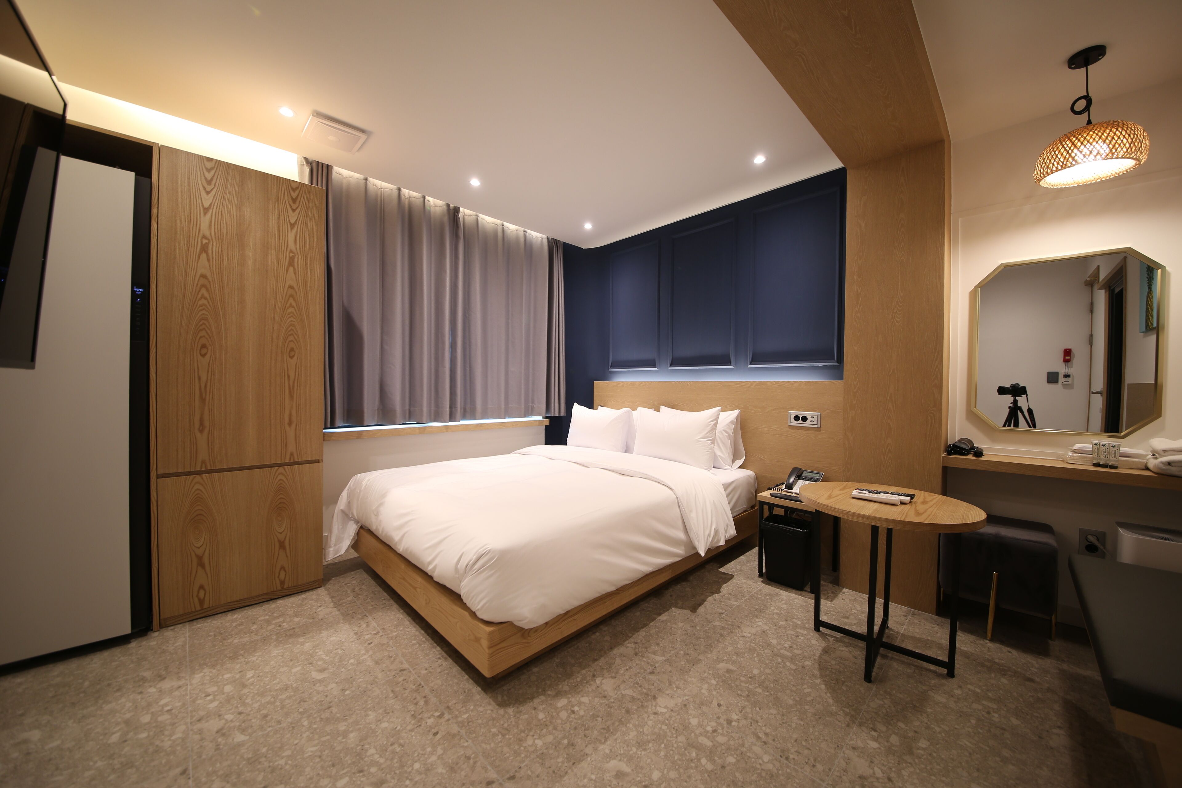 Ein modernes Hotelzimmer mit einem hölzernen Bett, einem kleinen Schreibtisch, einem Spiegel und einem Fenster mit Vorhängen.