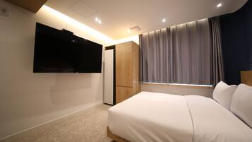 Une chambre à coucher avec un lit, un téléviseur fixé au mur, une armoire et une fenêtre avec des rideaux.