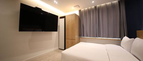 Una camera da letto con un letto, una TV montata a parete, un armadio e una finestra con tende.