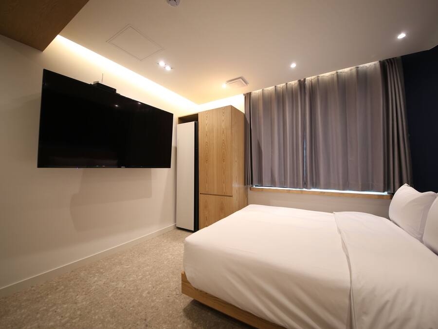 Une chambre à coucher avec un lit, un téléviseur fixé au mur, une armoire et une fenêtre avec des rideaux.