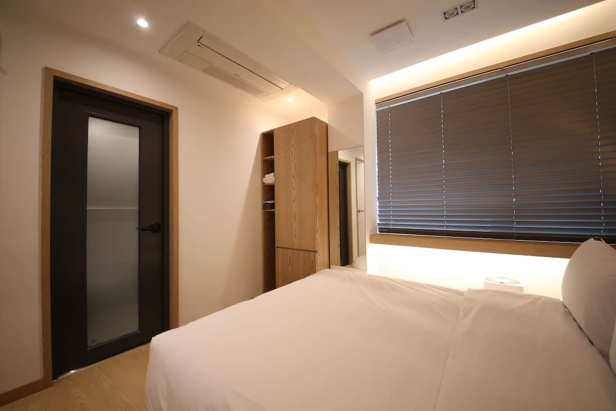 A bedroom with a bed, a wardrobe, a door, and a window with blinds.