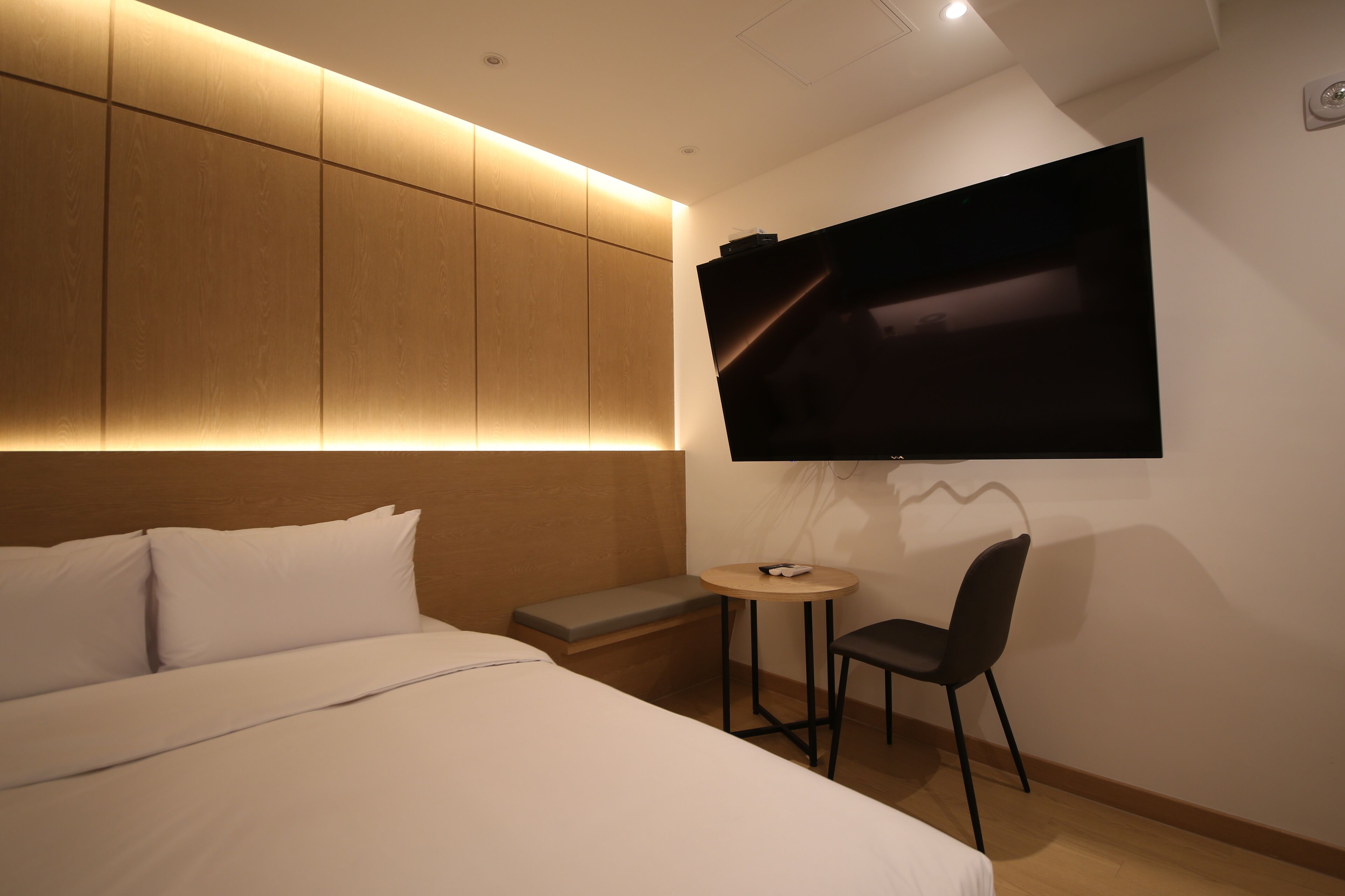 A modern hotel room with a large bed, a small table, a chair, and a TV mounted on the wall.