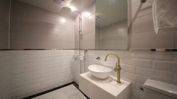 Ein modernes Badezimmer mit weißen, rechteckigen Fliesen, einem weißen Waschbecken mit Goldarmatur und einer Handbrause.