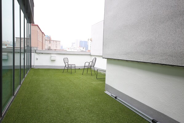 A rooftop terrace with artificial grass, two chairs, and a glass wall overlooking a cityscape. - Vantt Hotel (Gwangju)