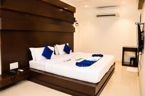 A hotel room with a large bed, a bedside table with a phone, an air conditioning unit, and a small shelf. - Hotel Mahendra (Raipur)