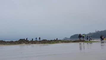 A beach with people walking on the sand and a rocky area in the background.