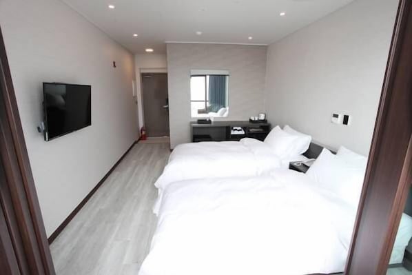 A modern hotel room with a large bed, a flat-screen TV mounted on the wall, a desk with a chair, and a small window.