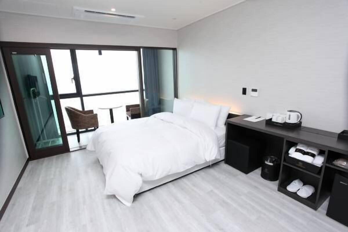 A modern hotel room with a large bed, a desk with a coffee maker, and a shoe rack.