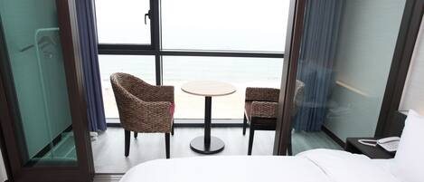 Habitación de hotel con cama, una mesita redonda pequeña, dos sillas de mimbre, un teléfono en una mesita de noche y vistas al mar a través de ventanas grandes.