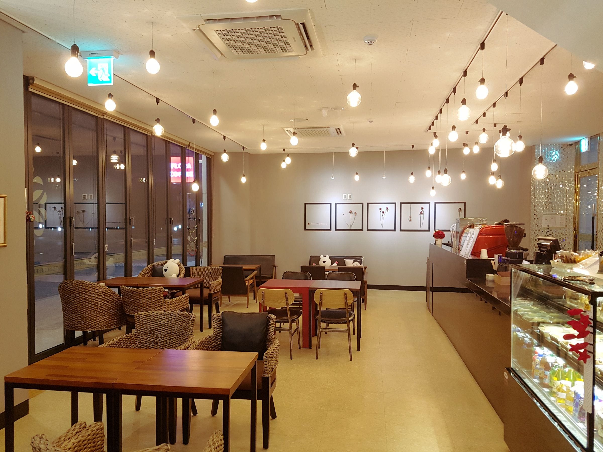 A restaurant interior with wooden tables and chairs, hanging light bulbs, and framed pictures on the wall.