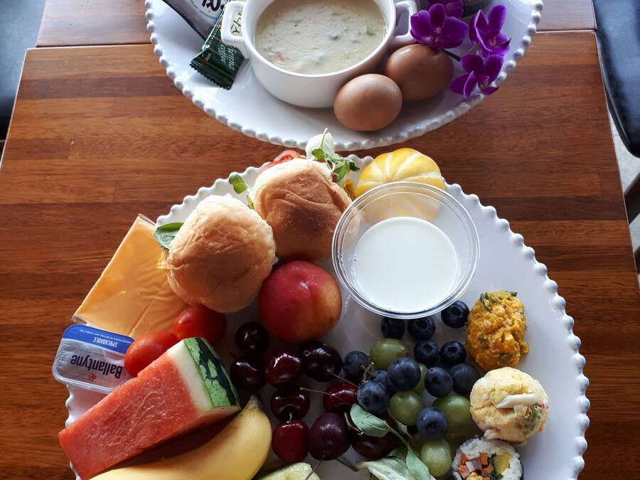 A breakfast tray with eggs, toast, fruit, yogurt, and a cup of soup.