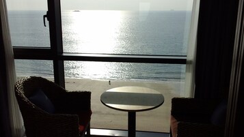 A room with a large window overlooking a beach, a small round table, and two wicker chairs.