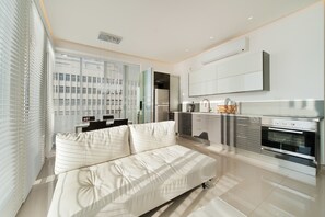 A modern kitchen with a built-in oven, a dining area with a table and chairs, and a large window with blinds.