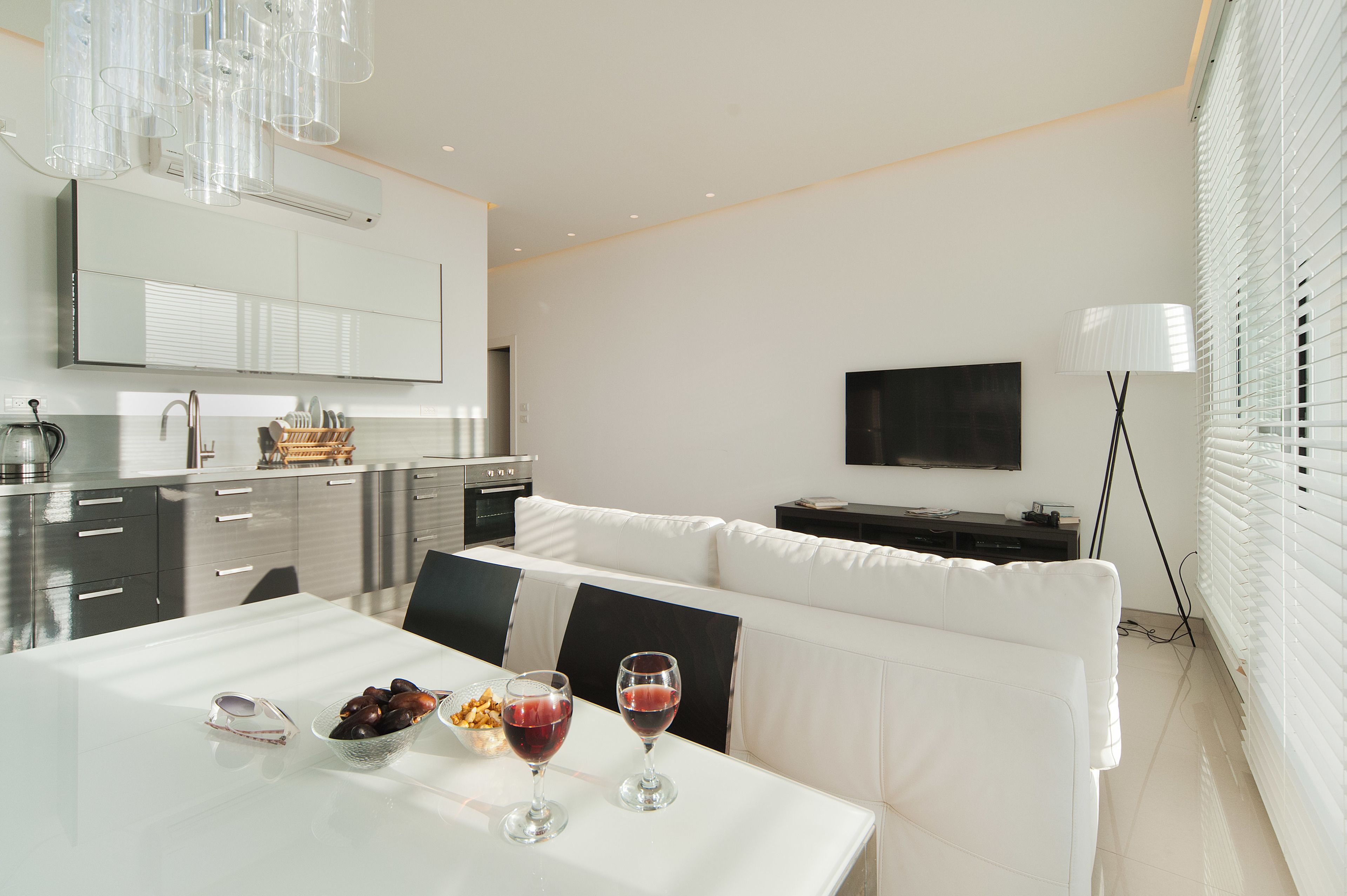 Una cocina moderna con comedor, muebles blancos y un televisor montado en la pared.