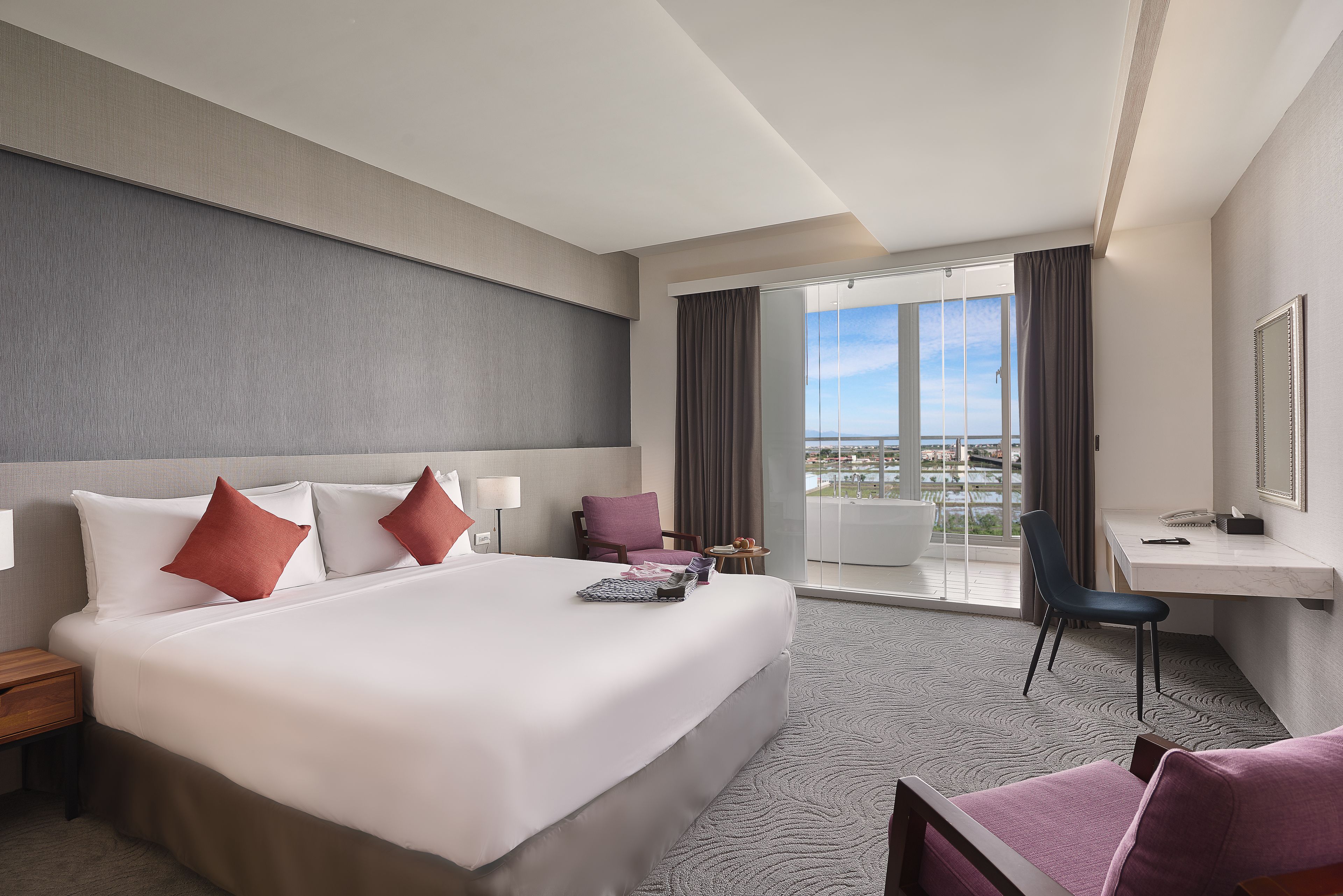 Habitación de hotel con una cama grande, un escritorio, una silla y vistas a la ciudad.