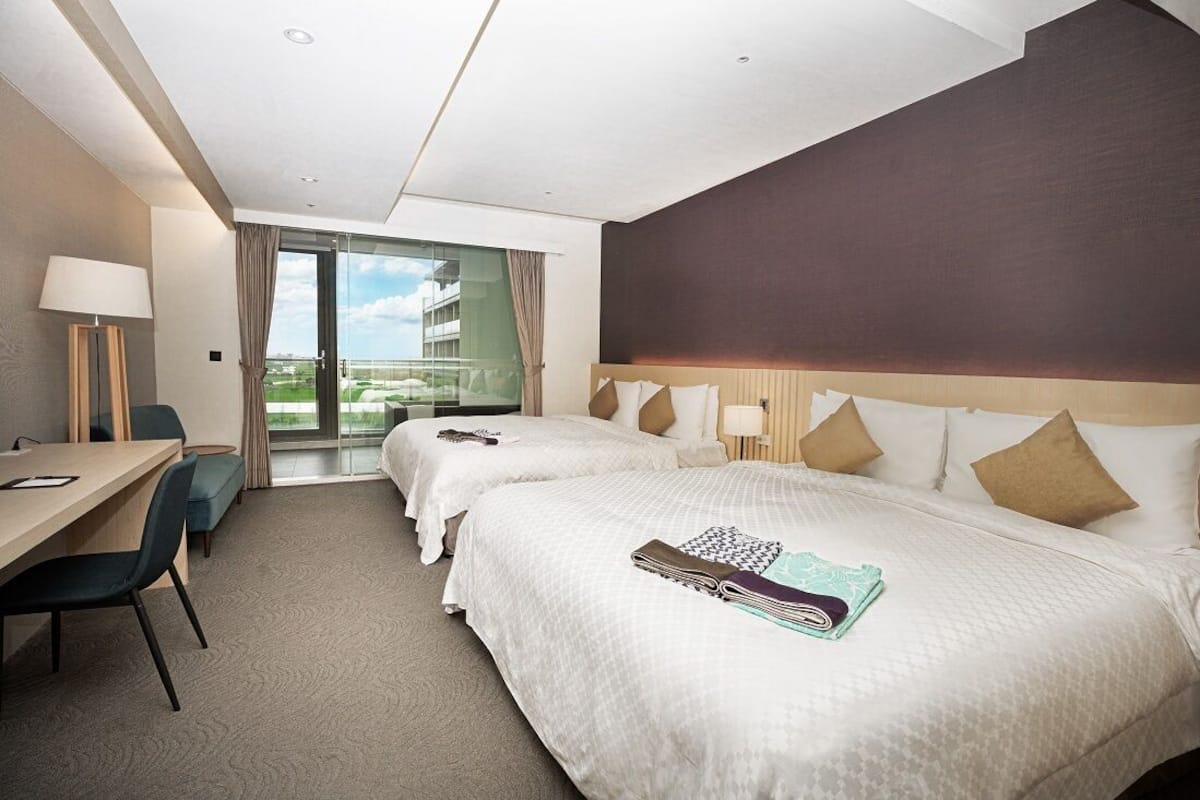 Une chambre d’hôtel avec deux lits, un bureau et une vue sur l’extérieur.