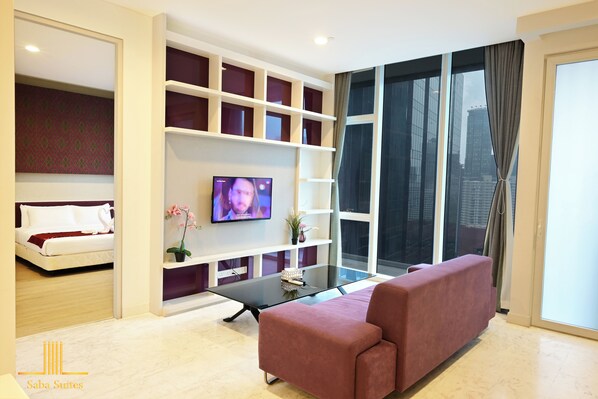 A modern living room with a sofa, a TV, a glass coffee table, and a large window with curtains. - Saba Suites at Platinum KLCC Kuala Lumpur (Kuala Lumpur)