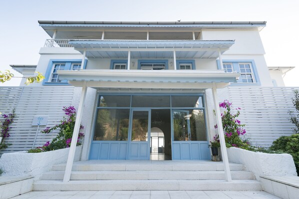 A two-story building with a balcony on the upper floor, a large glass entrance, and steps leading up to the entrance. - Thea Butik Hotel & Restaurant (Seferihisar)
