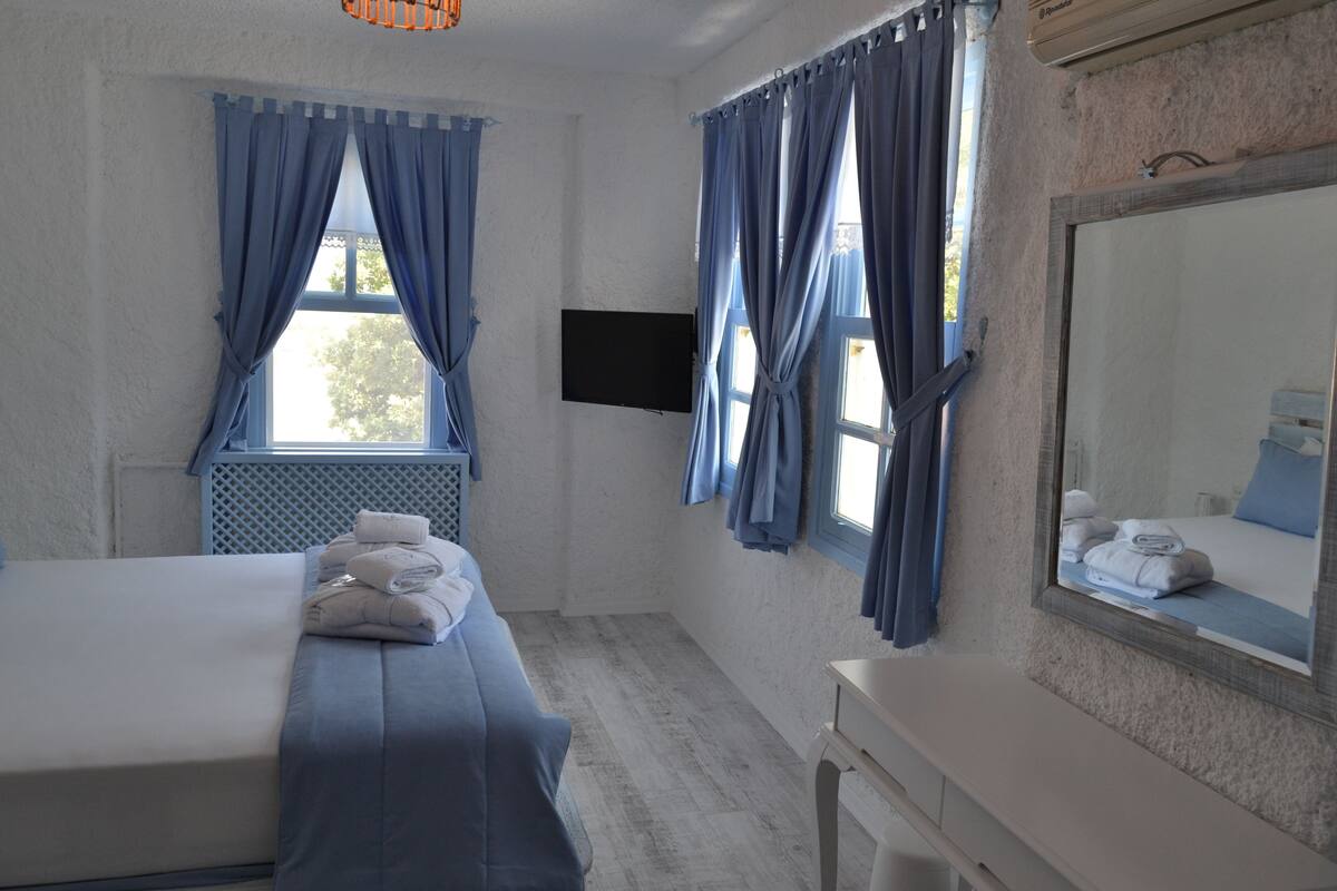 A hotel room with a bed, a desk, a mirror, and a TV.