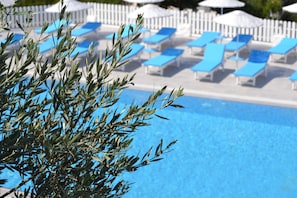 A pool area with blue lounge chairs and umbrellas, surrounded by a white fence. - Thea Butik Hotel & Restaurant (Seferihisar)