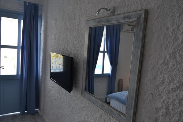 A room with a mounted flat-screen TV, a large mirror, and a window with blue curtains. - Thea Butik Hotel & Restaurant (Seferihisar)