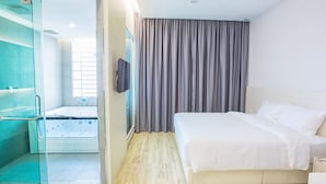 Habitació d'hotel moderna amb un llit gran, una zona de banyera amb dutxa tancada amb vidre i vistes a la ciutat.
