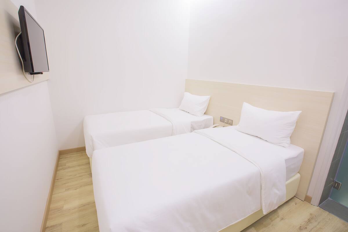 A hotel room with two single beds, a flat-screen TV mounted on the wall, and a wooden floor.