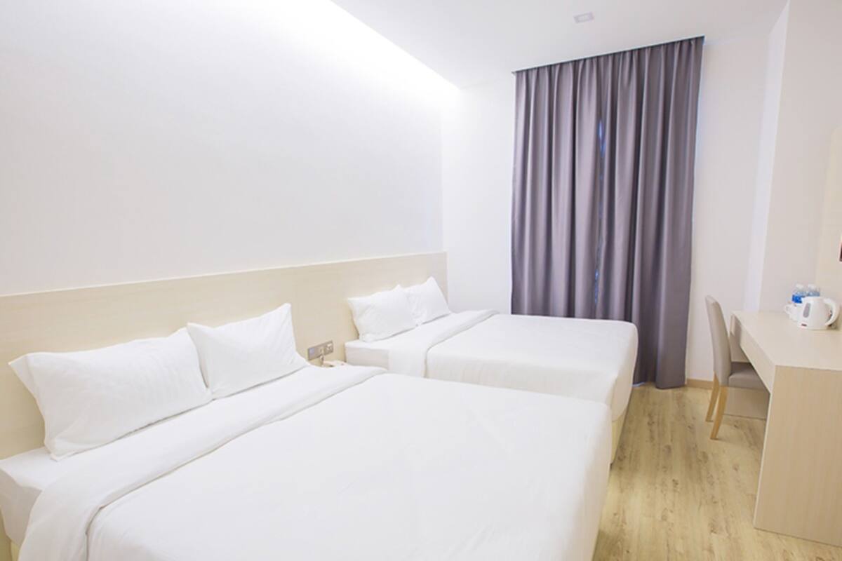 A hotel room with two single beds, a desk, and a chair.