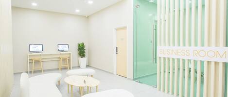 A business room with a white color scheme, two desks with computers, a potted plant, and a sign indicating the room's purpose.