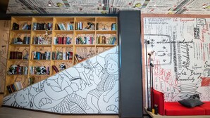 A cozy reading area with a large bookshelf filled with books, a colorful mural, and a comfortable red sofa.
