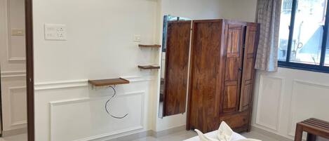 A room with a bed, wooden wardrobe, and a window with curtains.